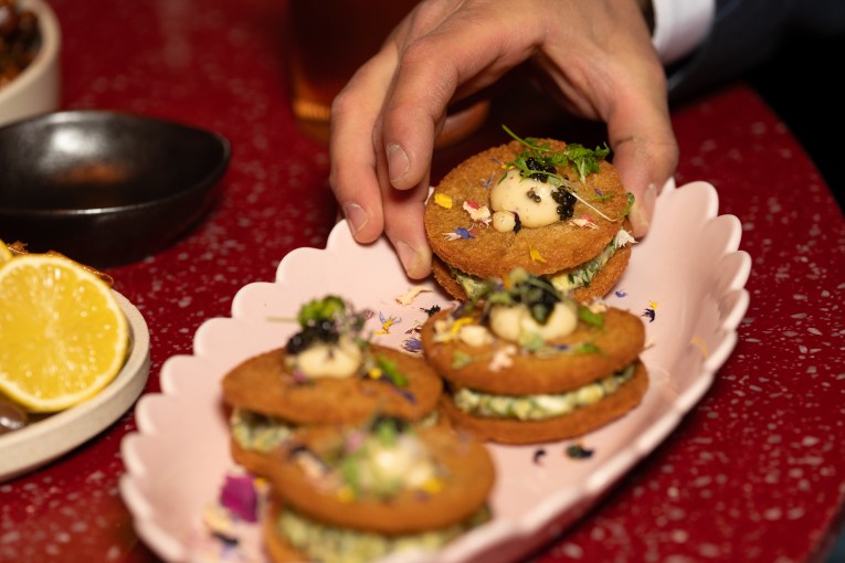 A hand reaches for an h'ors doeuvre on a pink scalloped plate