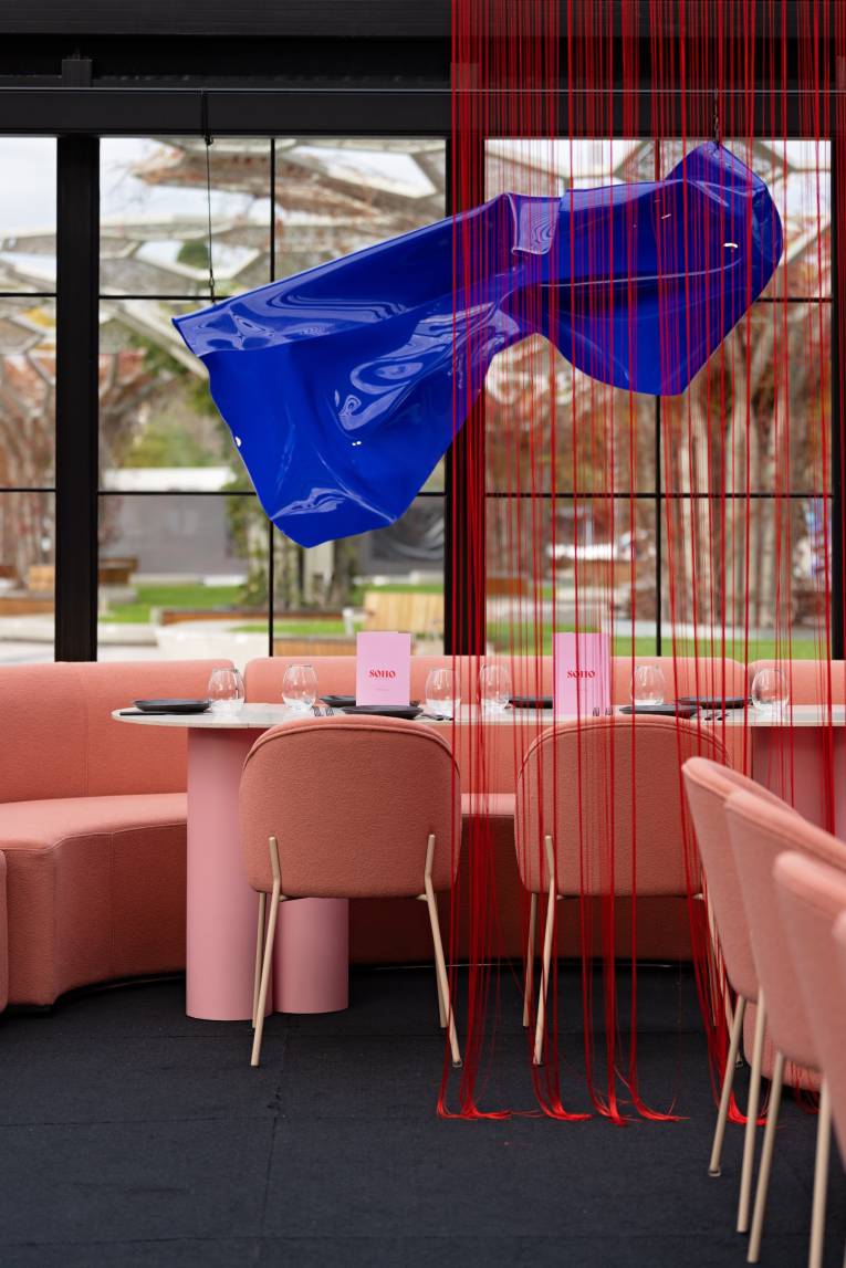 Pink upholstered chairs around a dining table set for a party with a blue organic shape above