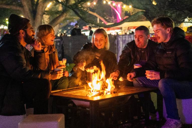 People gathered around a firepit and toasting marshmallows at Bastille Festival