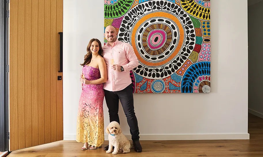 Stacey Lee with husband Ben Millar in front of a colourful piece by First Nations artist Debra Nangala McDonald) has opted for bright styling in both her life and at her Mediterranean-themed dinner party.