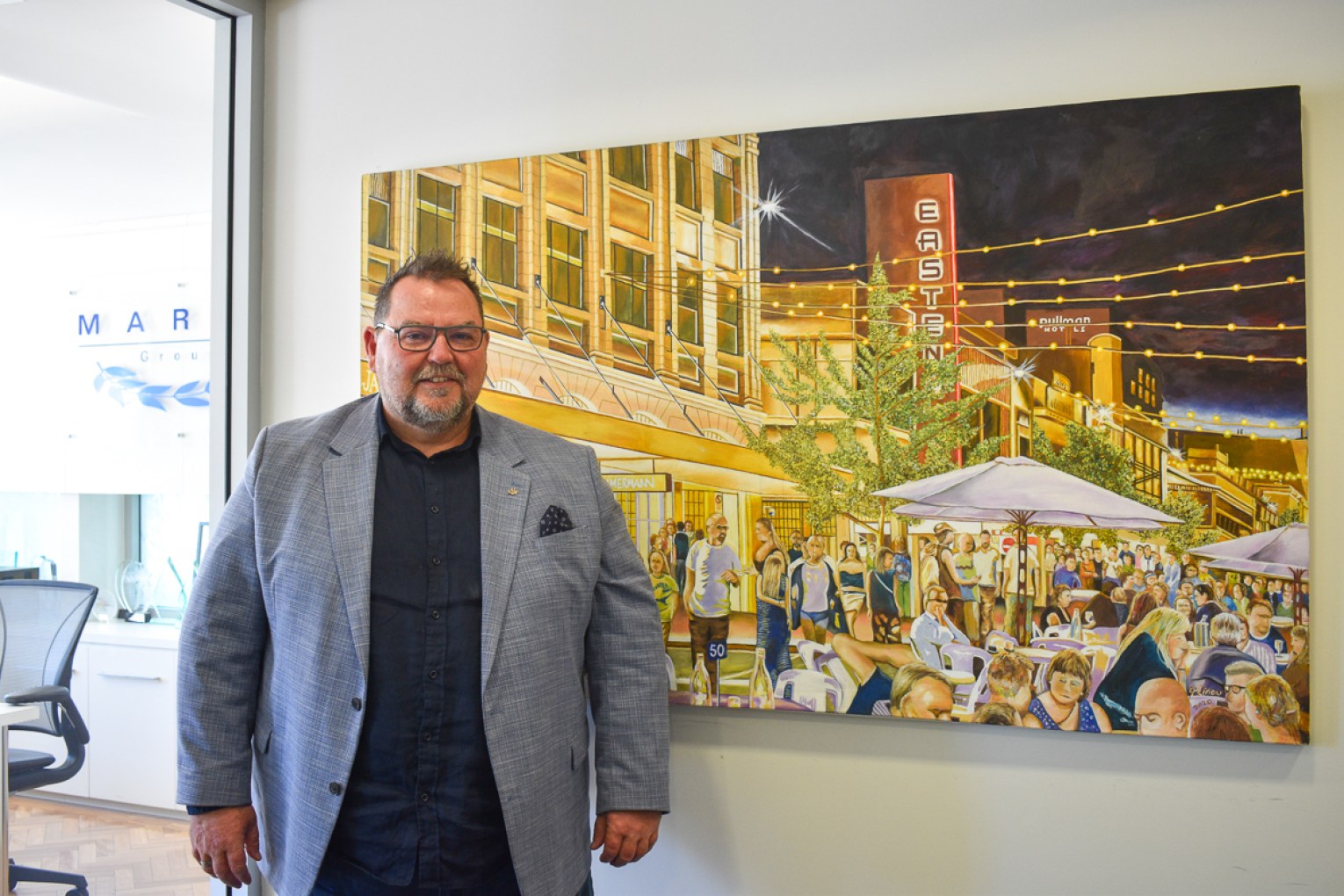 Steve Maras with a painting of a thriving east end by visual artist George Linou. This picture: Helen Karakulak/InDaily