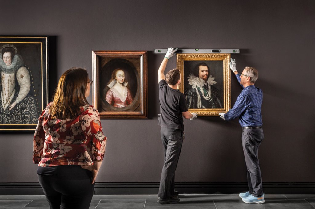 Curator Tansy Curtin watches on as installation team leader Harry Sadler and installation officer Ken Orchard install Michiel van Miereveld’s George Villiers, Duke of Buckingham.