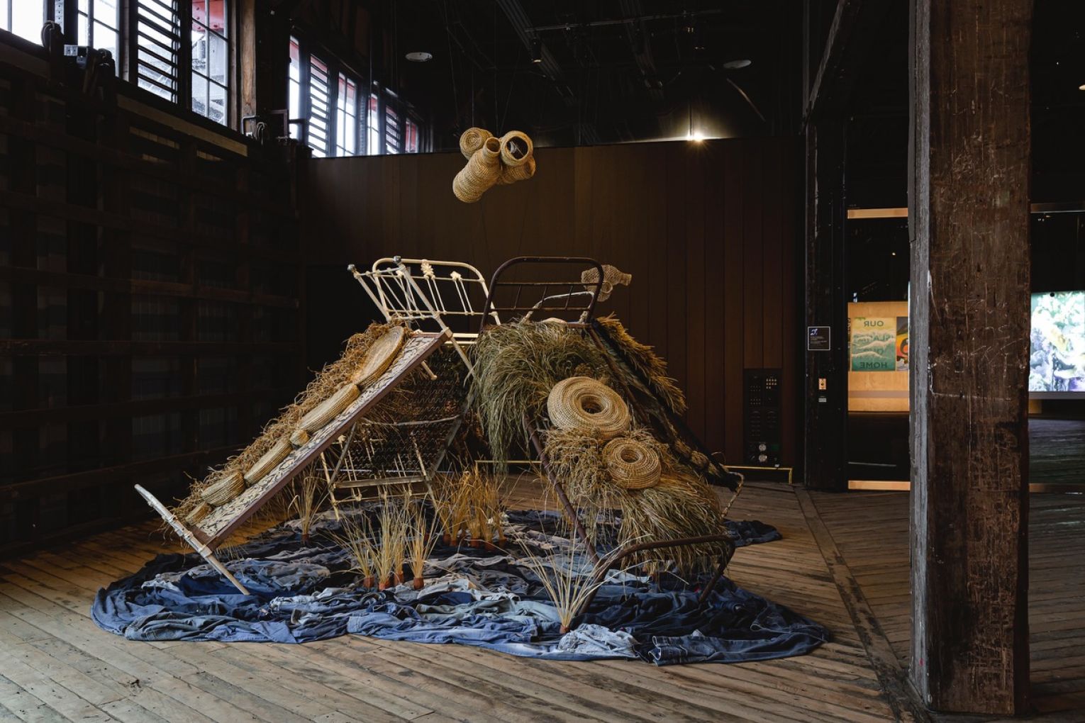 Casino Wake Up Time Slumber Party, 2022-24, antique beds; Australian native plants (buchie rush, bullrush, bracken fern, lomandra, eucalyptus, grass), weeds (umbrella sedge, setaria), terracotta clay, jute string, paper wire twist ties, secondhand denim. Photo: Courtesy of Biennale of Sydney