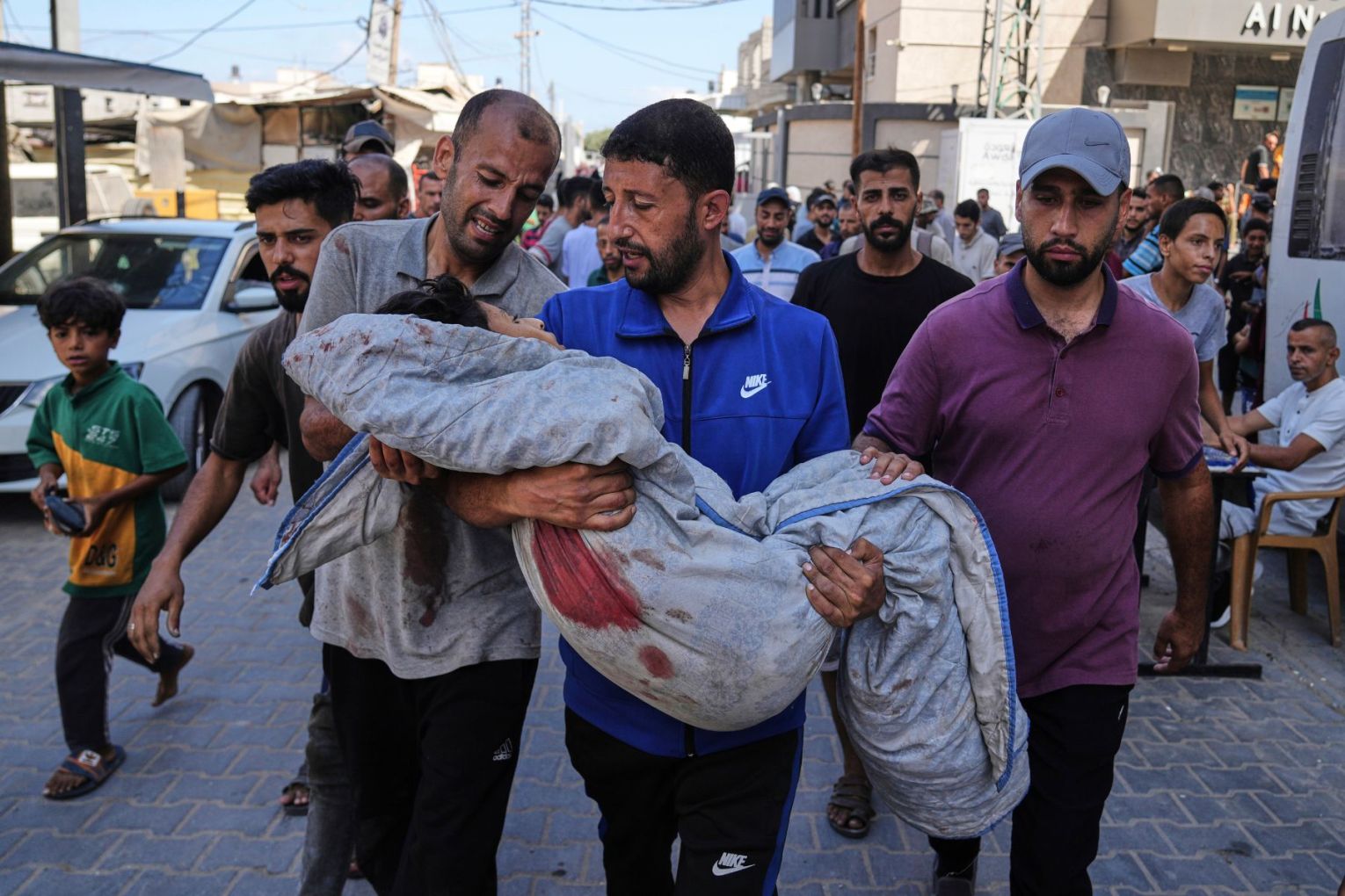 Relatives carry the body of 13-year-old Seraje Ebrahim, killed in an Israeli strike on a drinking water distribution point, for burial outside Al-Awda Hospital in Nuseirat, central Gaza Strip. Photo: Abdel Kareem Hana/AP.