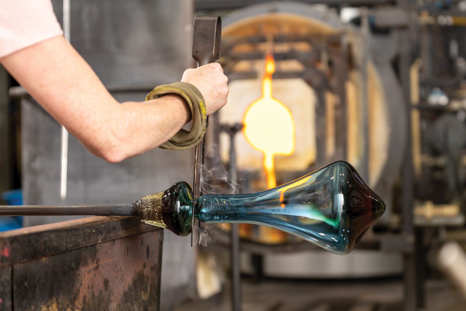 Emma snips the top of a wine decanter, which she has blown and sculpted from molten hot glass on JamFactory’s hot shop floor.