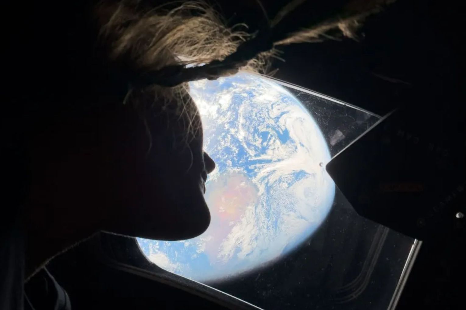 Christina Koch peers out the spacecraft's window, looking back at Earth. 